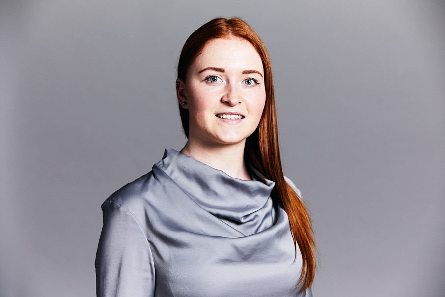 Corporate headshot of business woman with red hair in grey top