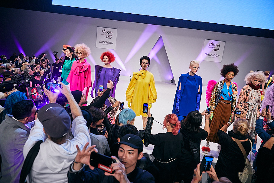 Vidal Sassoon fashion and hair show.  Models lined up on stage in bright colourful clothing. 